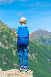 从背着背包的男孩旅行者站在岩石上看