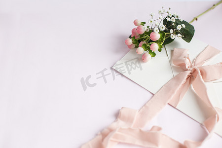 邀请函摄影照片_白色粉红色背景的信封，带有桃色丝带和粉红色花朵。