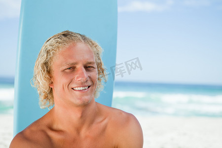 带着冲浪板坐在大海前微笑的年轻人