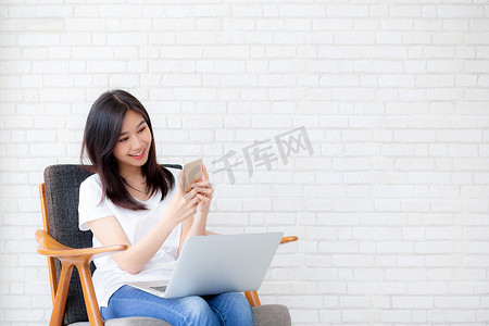 年轻的亚洲女性是自由职业者，坐在智能手机和笔记本电脑上工作，女孩的空闲时间在手机上放松和舒适，快乐和舒适，商业和技术，生活方式概念。