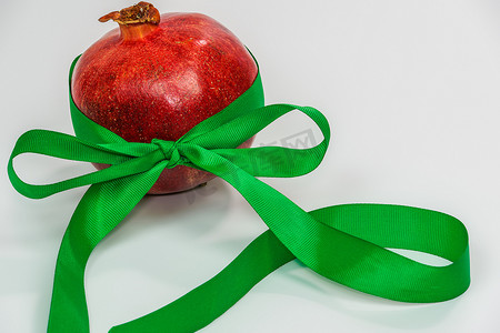 彩带装饰摄影照片_与绿色丝带的石榴作为白色背景的新年礼物。