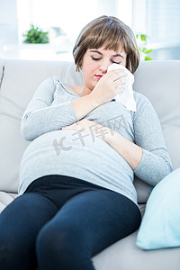 孕妇生病摄影照片_坐在沙发上要打喷嚏的孕妇