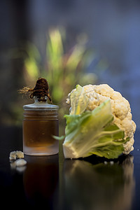 在黑色表面的一个小玻璃瓶中特写生花椰菜及其精油，有选择性的聚焦、创意照明和模糊的背景。