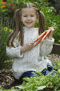 一个小女孩在花园里拿着胡萝卜的肖像