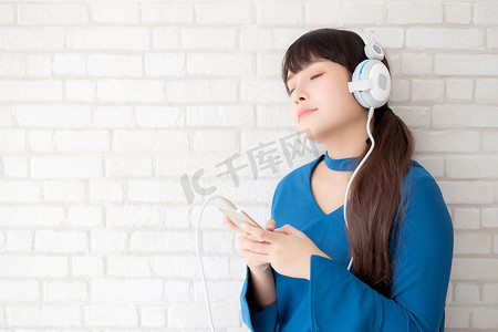 听收音机摄影照片_美丽的肖像亚洲年轻女性站在水泥混凝土背景上快乐地享受和享受耳机听音乐，女孩的生活方式用耳机放松收音机，技术概念。