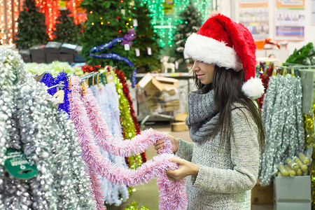 戴着圣诞帽的年轻女人在圣诞树上选择装饰品