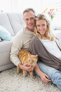 微笑的夫妇在地毯上抚摸他们的格林杰猫