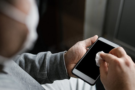 蒙面男子用酒精或消毒剂清洁智能手机屏幕。