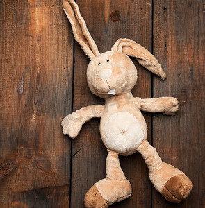 木质背景上长着大耳朵和滑稽脸的滑稽米色毛绒兔子