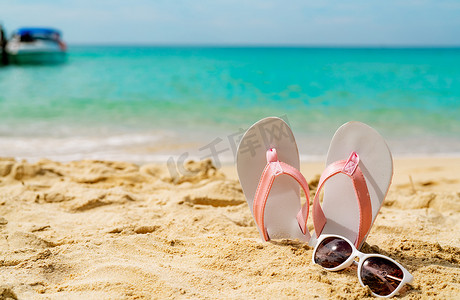 粉色和白色凉鞋，海边沙滩上的太阳镜。 