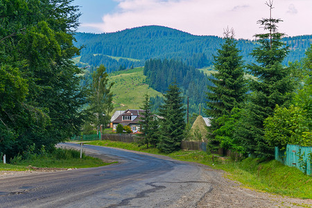 以农村房屋和巨大的绿色山脉为背景的陡峭蜿蜒的道路