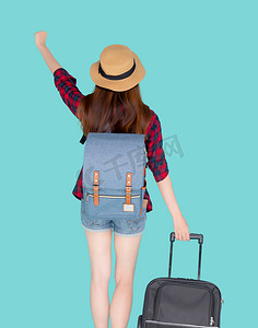 后视美丽的年轻亚洲女人拉着蓝色背景中突显的手提箱，有表情的亚洲女孩带着兴奋、旅行和旅行的概念快乐地拿着行李在假期中行走。