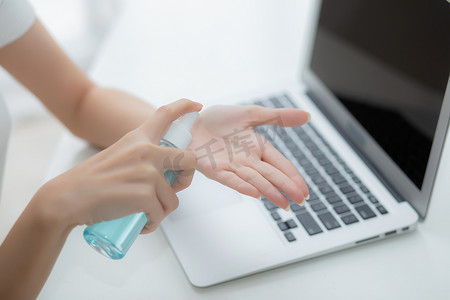 妇女的手在家工作，用酒精凝胶或消毒剂清洁手并保护冠状病毒或 covid-19，新常态，检疫和社会疏远，女商人使用笔记本电脑。