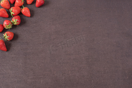 整个新鲜成熟的红草莓的边界排列在左侧，带有复制空间的深色纹理石板背景上。