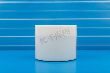 蓝色背景下蓝色桌子上无品牌的白色亮面霜、香脂、面膜或其他美容产品罐的特写