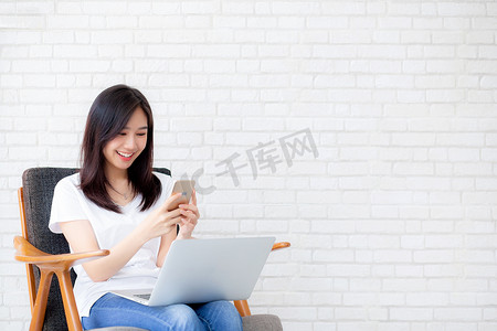 年轻的亚洲女性是自由职业者，坐在智能手机和笔记本电脑上工作，女孩的空闲时间在手机上放松和舒适，快乐和舒适，商业和技术，生活方式概念。