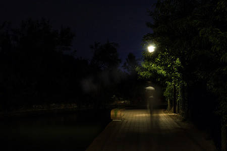 照亮黑暗摄影照片_人在黑暗的街道上行走的双重曝光夜景被路灯照亮。