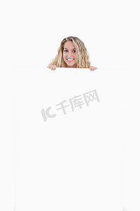 微笑的年轻女人把她的身体藏在一张空白的海报后面