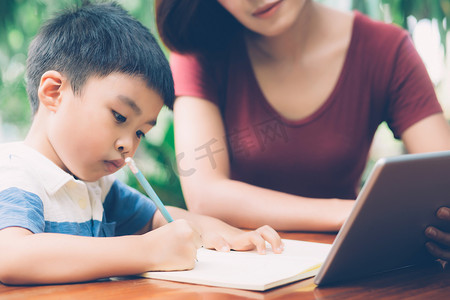 儿子使用数字平板电脑学习和学习与母亲一起在线上网、家庭教育、家庭娱乐、妈妈教男孩和家庭作业与技术、生活方式概念。