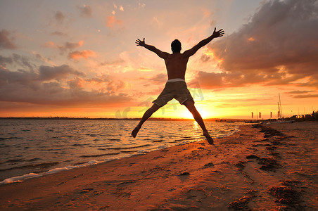 相信光摄影照片_张开双臂的年轻人在日落时分在海边庆祝和享受这一刻