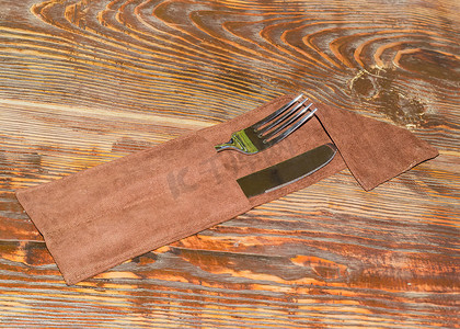 餐具刀和叉摄影照片_旧木桌上餐具袋中的叉子和刀