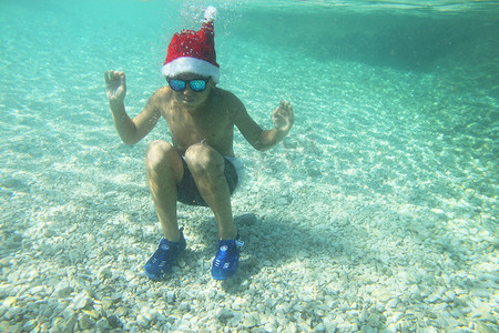 戴圣诞帽的男孩摄影照片_戴着圣诞帽的男孩在海中游泳