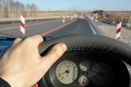 正在修护围栏的道路背景下，司机把手放在汽车的方向盘上