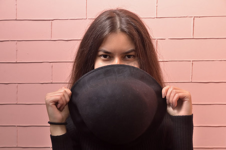 一个年轻女孩的肖像特写，她在深红色的砖块背景上拿着一顶黑帽子