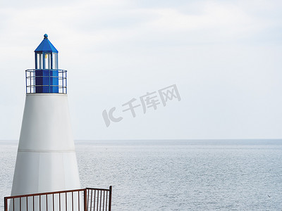 有蓝色塔的白色灯塔在灰色平静的海背景。