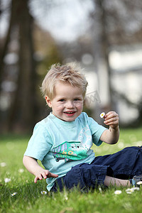 坐在绿色草地上的快乐金发小男孩