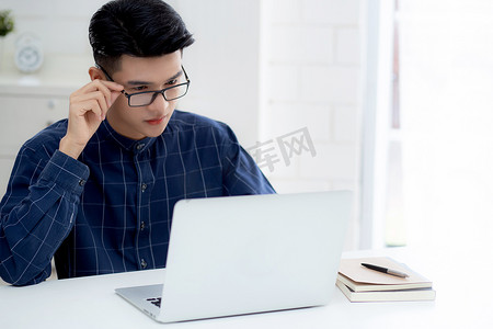 戴眼镜的年轻商人在家工作，办公桌上放着笔记本电脑，自由职业男性坐在家里，用笔记本电脑在桌上交流，创业企业家，新常态。