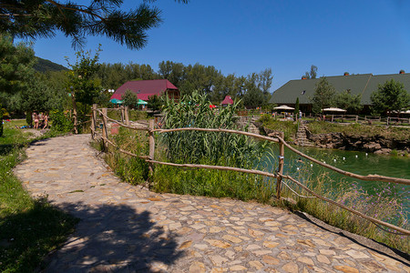 大池塘摄影照片_带大池塘的休闲公园，小径两旁铺着砖砌楼梯，通往水上小屋，供人们在炎热的夏日阳光下休息。