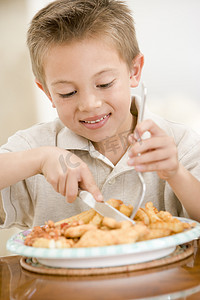 儿童吃鱼摄影照片_室内吃炸鱼薯条微笑的小男孩