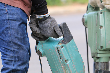 男性工人使用电动混凝土破碎机在当地城市道路、人行道、工作施工现场用手提钻挖掘和钻孔混凝土修复车道表面。
