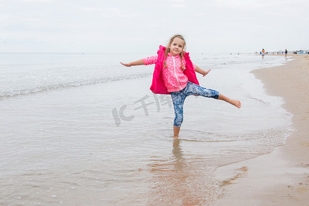 玩乐的三岁女孩单腿站在沙滩上