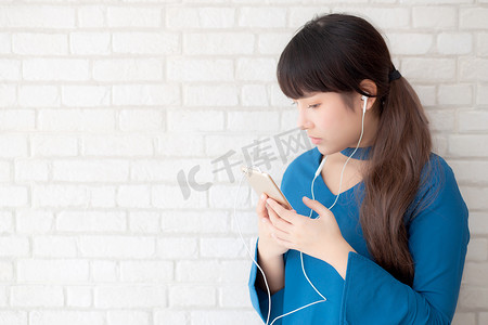 美丽的肖像亚洲年轻女性站在水泥混凝土背景上快乐地享受和享受耳机听音乐，女孩的生活方式用耳机放松收音机，技术概念。