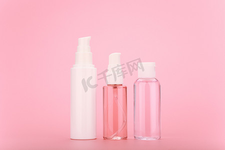 亮面背景摄影照片_透明瓶中的面霜、清洁泡沫或凝胶和乳液，白色瓶盖，亮粉色背景