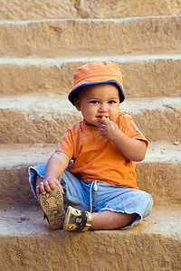 穿着橙色衣服的男孩坐在台阶上吃东西