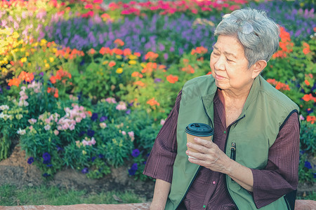 亚洲老年老年妇女在花园里喝咖啡茶。