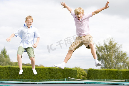 开心跳跃的小男孩摄影照片_跳跃在蹦床上微笑的两个小男孩