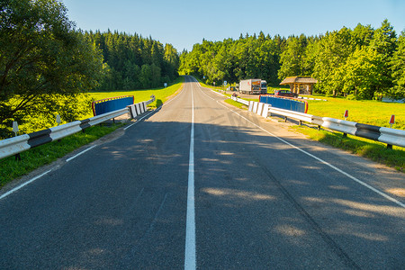关卡摄影照片_一条双车道公路，位于明亮的绿色林带和蓝天之间