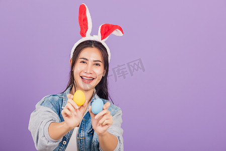 戴着兔耳和牛仔布微笑的女人手上拿着彩色复活节彩蛋礼物