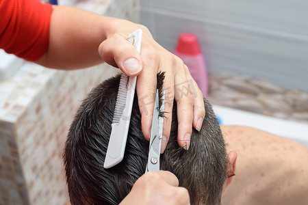 客户家里摄影照片_理发师剪了一个男人头上的头发，在家里从浴室里的客户那里工作
