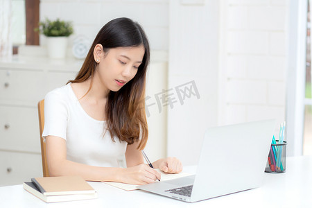 年轻的亚洲女性在笔记本上写作以计划工作和在家里的办公桌上使用笔记本电脑，关于金融、女性学习和学习、商业和沟通概念的女孩笔记。