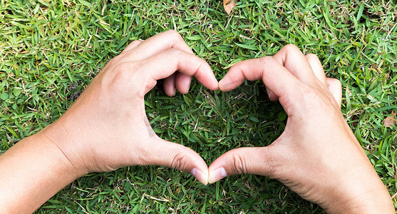 手心摄影照片_在绿草上塑造爱情概念的特写手心