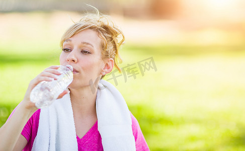 年轻健康的成年女性在户外用毛巾从她的水瓶里喝水。