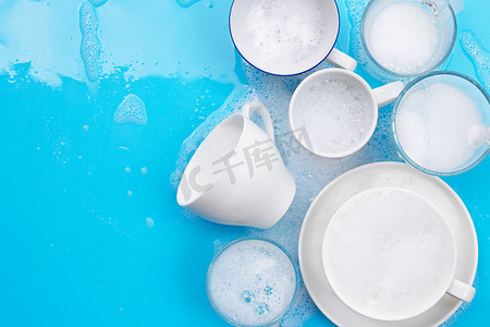 用肥皂泡沫在湿蓝色背景上清洗用过的饮水杯和杯子