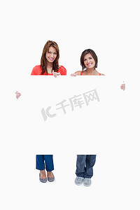 海报少女摄影照片_两个微笑的少女拿着一张空白的海报反对白色