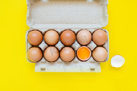 特写镜头在黄色背景上并排放置的纸盒中破裂了棕色鸡蛋和鸡蛋。
