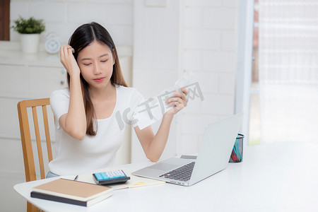 年轻的亚洲女性计算家庭财务费用，在家里的办公桌上感到沮丧，女孩检查账单有压力和担心、债务和税收、表达和情感、商业理念。
